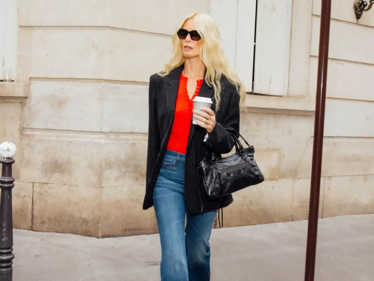Une femme blonde en lunettes de soleil, portant un blazer rayé, un haut rouge vif et un jean évasé. Un exemple parfait de que mettre avec un jean pour un look chic.