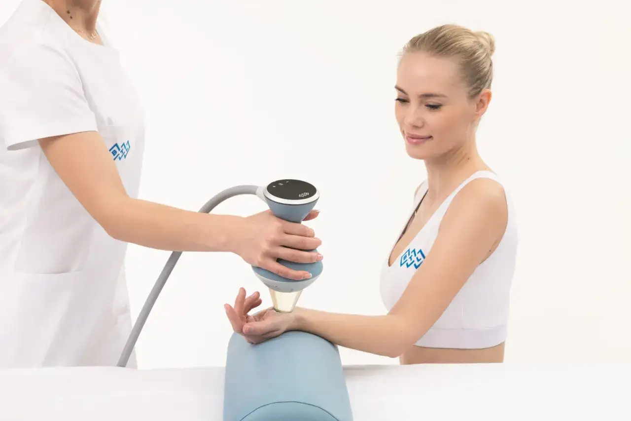 Terapia falą uderzeniową na nadgarstku. Terapeuta wykonuje zabieg na dłoni pacjentki.