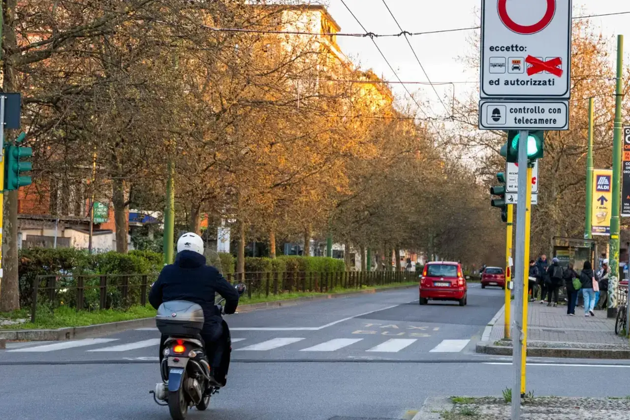 Un motorino attraversa un incrocio con semaforo verde, vicino a un cartello che indica il rispetto dell'art. 175 cds per l'accesso alla zona.