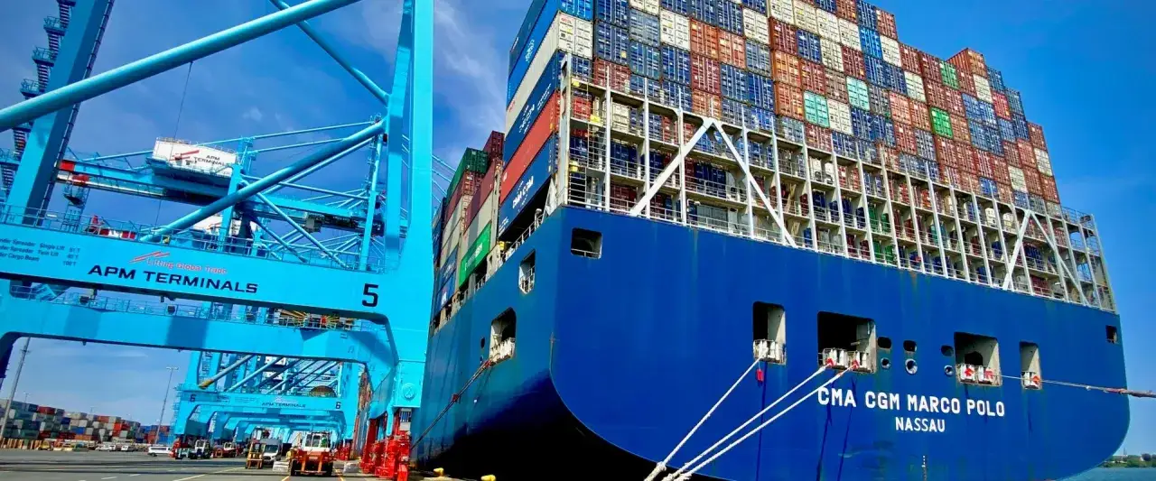 Un immense navire, le CMA CGM Marco Polo, est amarr&eacute; &agrave; quai, pr&ecirc;t &agrave; &ecirc;tre d&eacute;charg&eacute; par une super porte conteneur bleue d'APM Terminals.