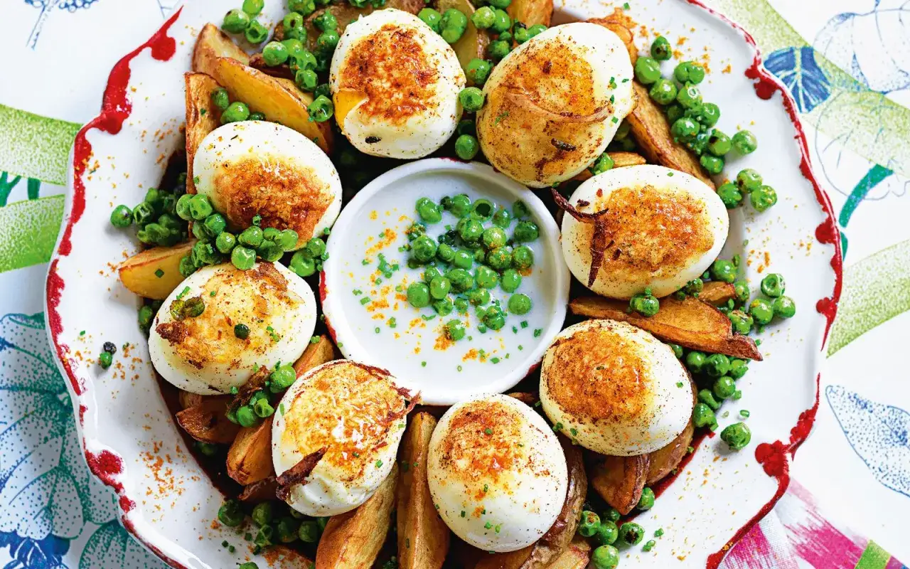Uova ripiene pasquali dorate, servite con patate arrosto e piselli freschi, un piatto colorato e gustoso.