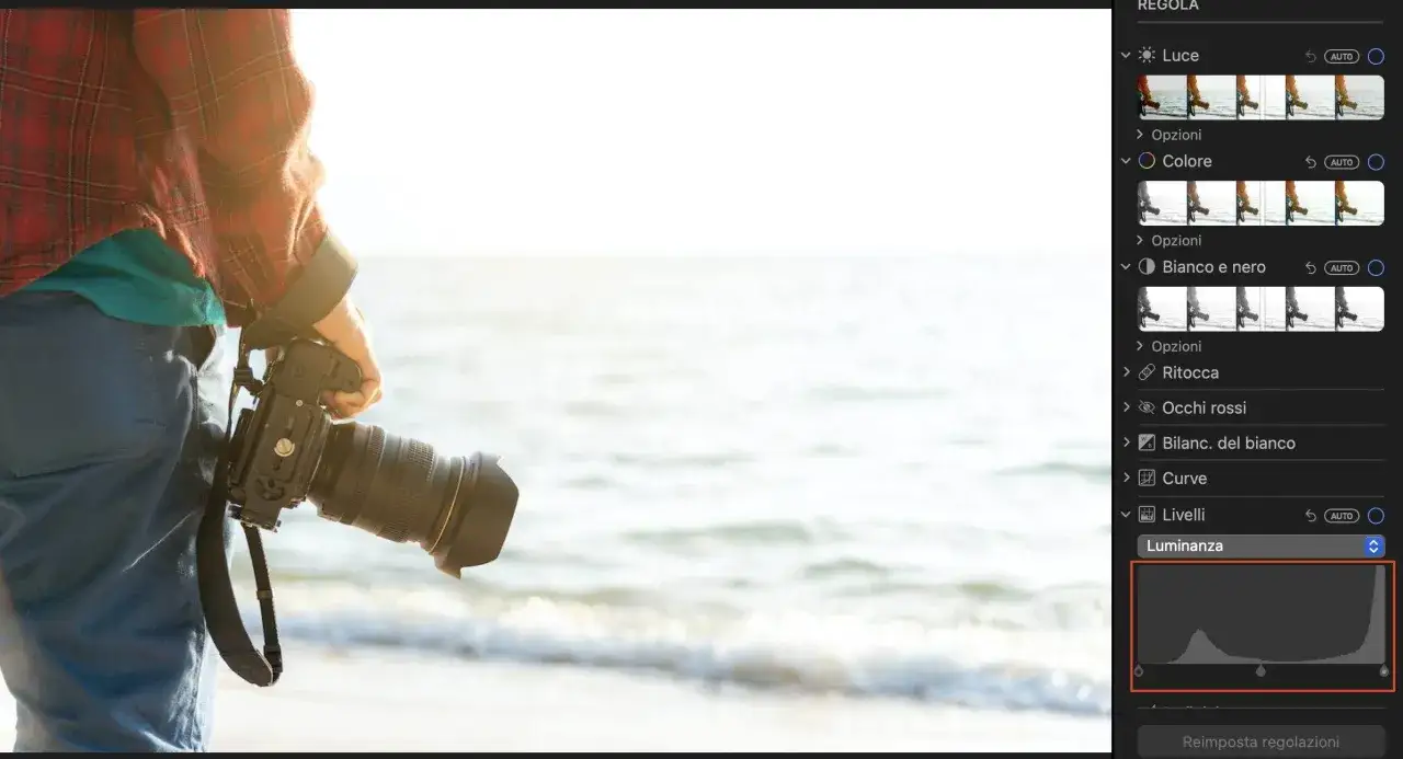 Un fotografo con una reflex sulla spiaggia, mentre impara come esporre fotografie usando i livelli di luminanza in un software di editing.