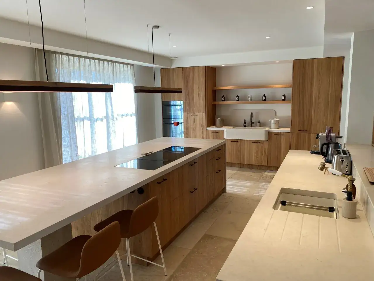 Exemple de cuisine moderne avec &icirc;lot central, plan de travail en pierre, placards en bois et &eacute;clairage suspendu.