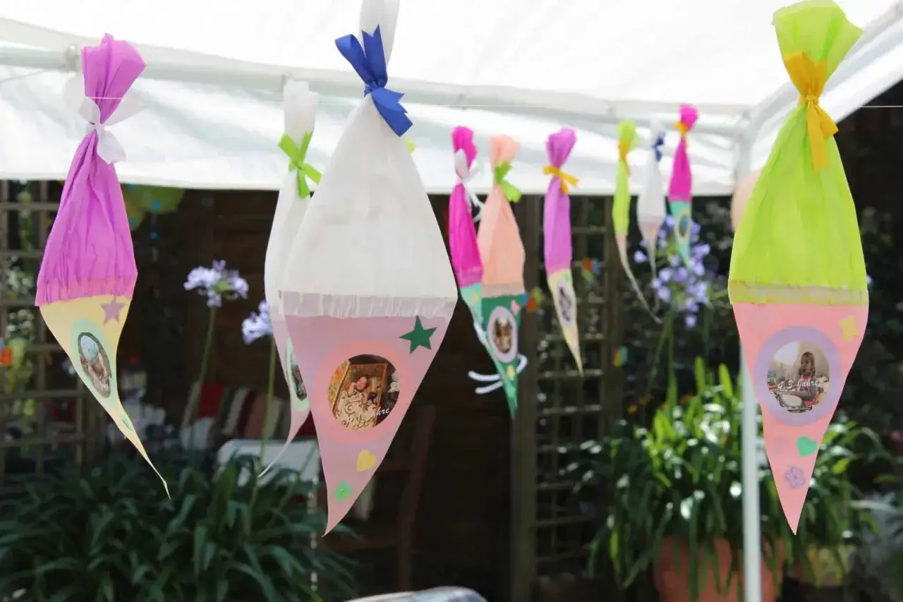 Bunte Zuckertüten mit Fotos hängen im Garten, bereit für die Einschulung.