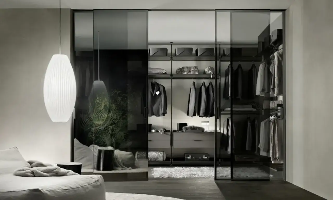 Una moderna cabina armadio fai da te con ante scorrevoli in vetro, abiti ordinati e un'elegante lampada a sospensione.