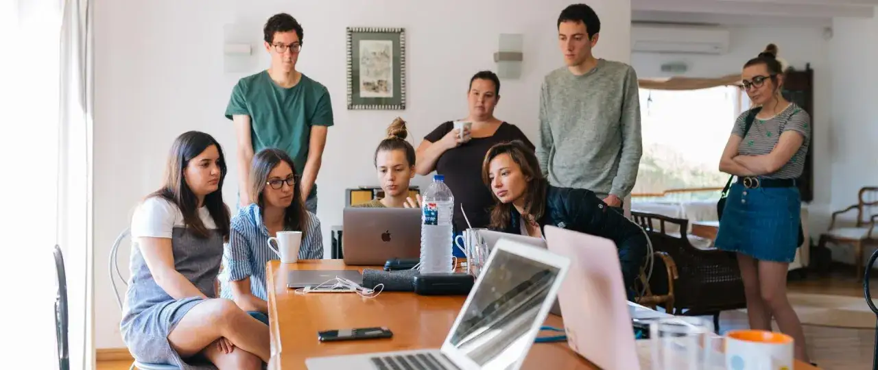 Grupa młodych ludzi pracuje przy laptopach. Dyskusja o tym, od ilu lat można pracować, trwa.