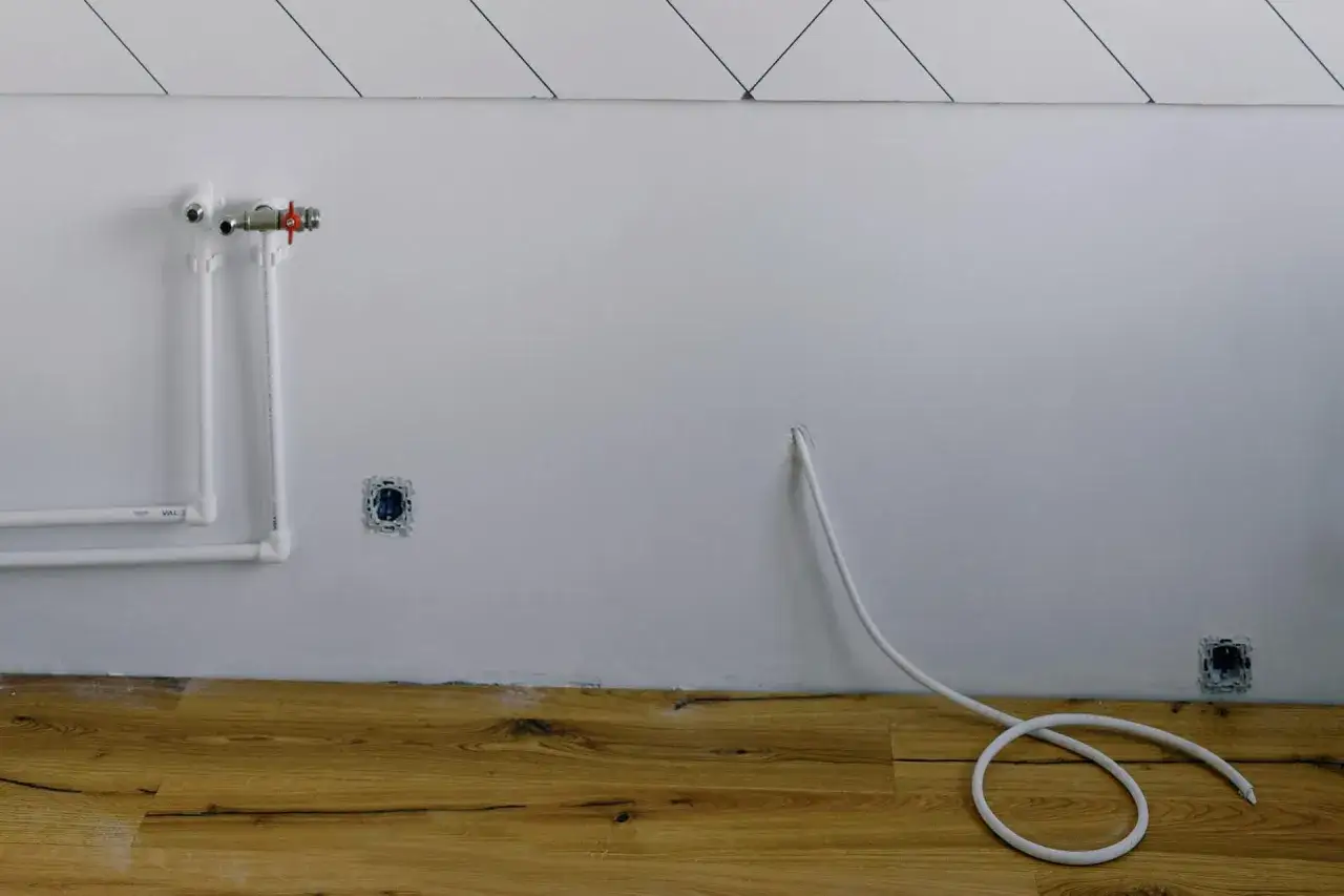 Białe rury gazowe w mieszkaniu, przygotowane do montażu. Obok gniazdka elektryczne i biały kabel.