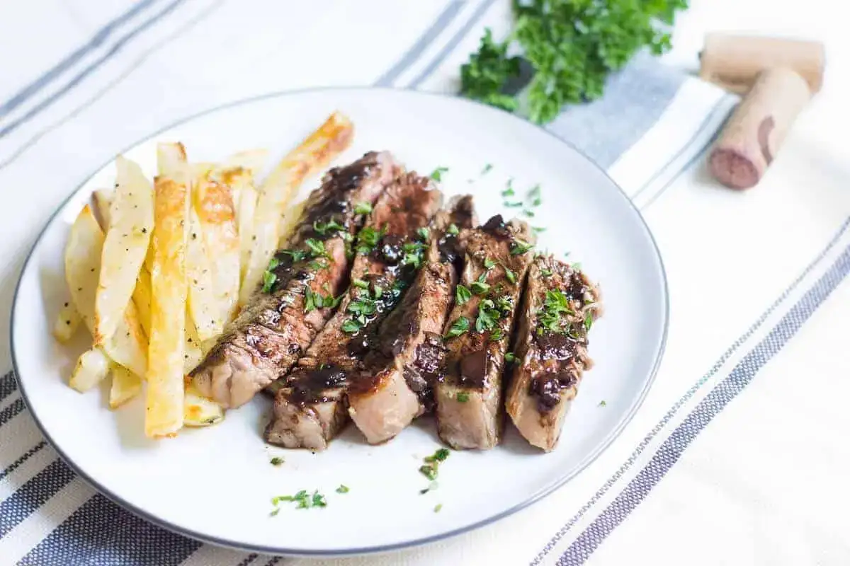 Skivad entrecote med perfekt innertemp, serverad med krispiga pommes frites och en mörk sås.