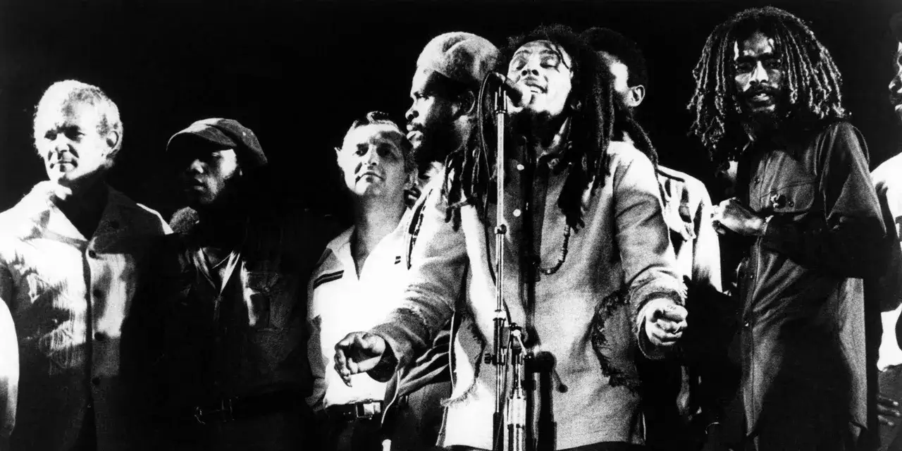 Bob Marley śpiewa reggae z zespołem na scenie.