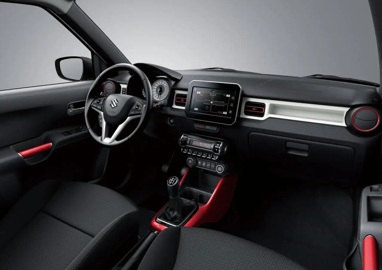 Interni moderni della Suzuki Ignis 2026 con touchscreen, sedili in tessuto e dettagli rossi vivaci.