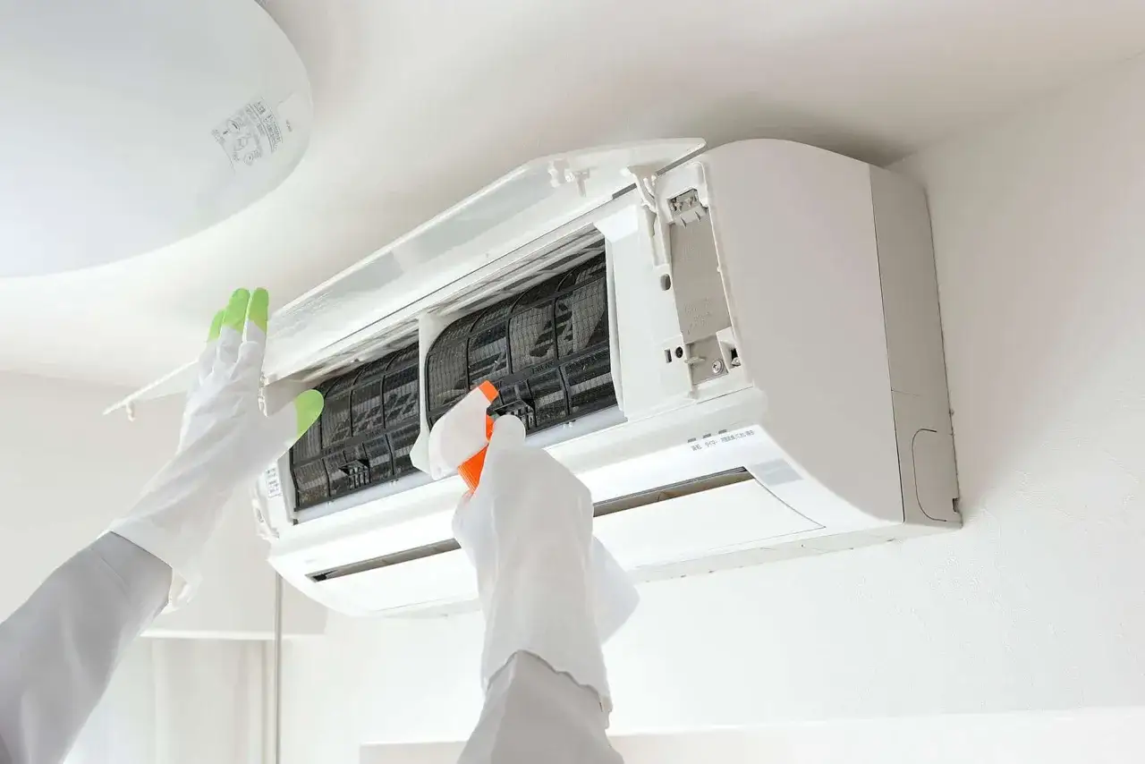 Maintenant, je nettoie l'évaporateur clim. avec un spray. Mes mains gantées s'occupent de cette tâche essentielle pour un air pur.