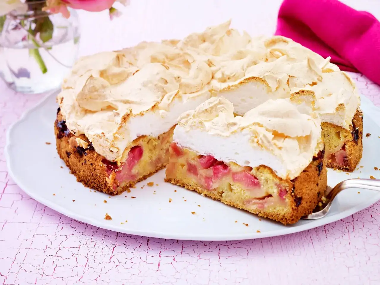 Ein saftiger Rhabarberkuchen mit einer luftigen Baiserhaube, auf einem weißen Teller, bereit zum Genießen.