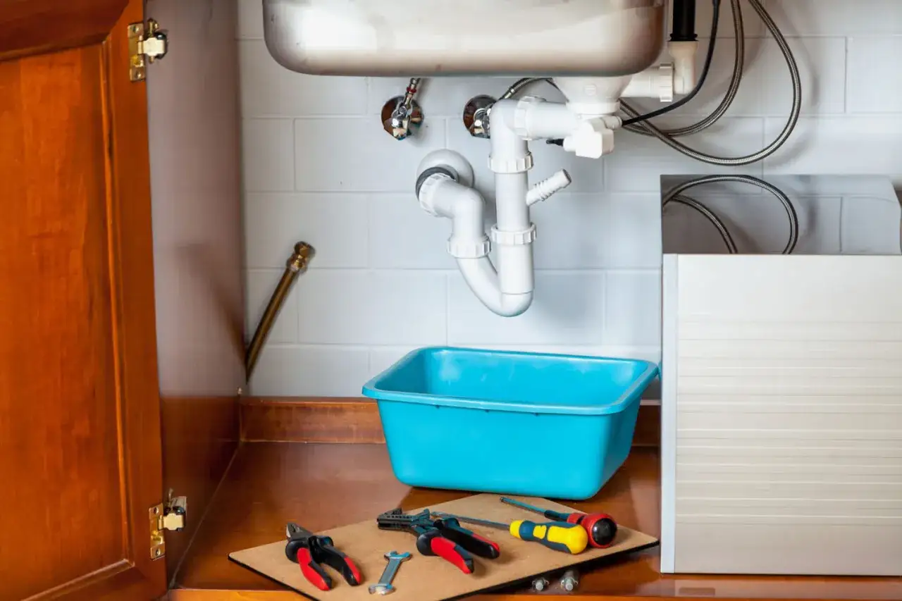 Outils et bac bleu pr&ecirc;ts pour d&eacute;boucher &eacute;vier. Plomberie sous l'&eacute;vier visible.
