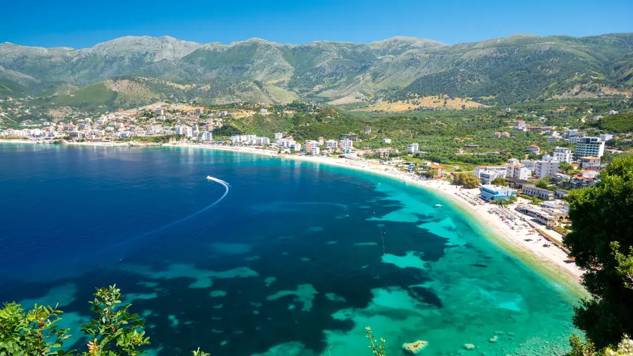 Malownicze albania plaże z turkusową wodą, białym piaskiem i zielonymi wzgórzami w tle. Widok na zatokę z łodzią na wodzie.