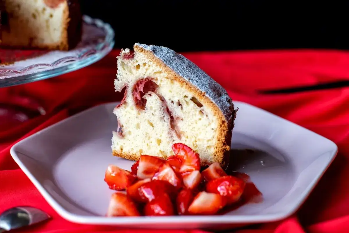 Un trozo de bizcocho de fresa esponjoso, espolvoreado con azúcar glas, acompañado de fresas frescas cortadas en un plato.
