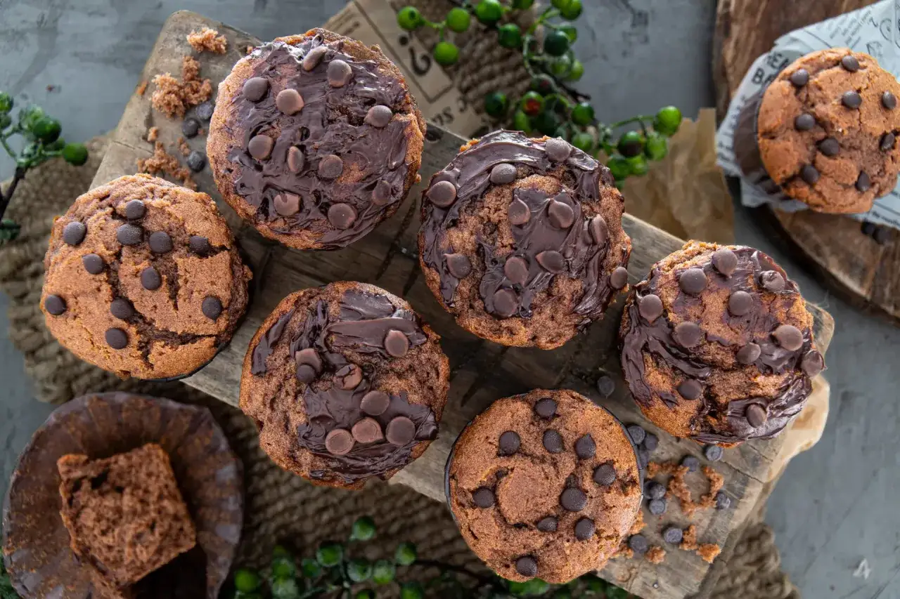 Saftige Nutella Muffins mit Schokost&uuml;ckchen, auf einem Holzbrett arrangiert. Ein Muffin ist angeschnitten und zeigt die feine Krume.