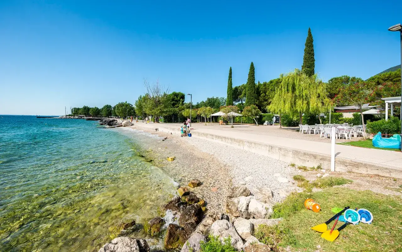 Słoneczny dzień na plaży w Toscolano. Czysta woda, kamieniste wybrzeże i zielone drzewa tworzą idealne miejsce na wakacje z rodziną.