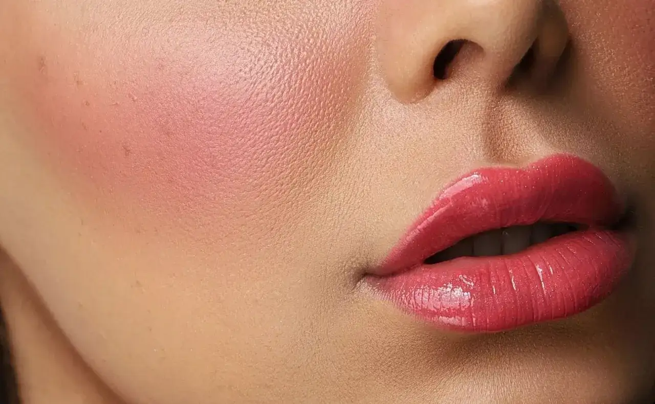 Błyszczące, pełne usta w stylu russian lips, z różowym rumieńcem na policzku.