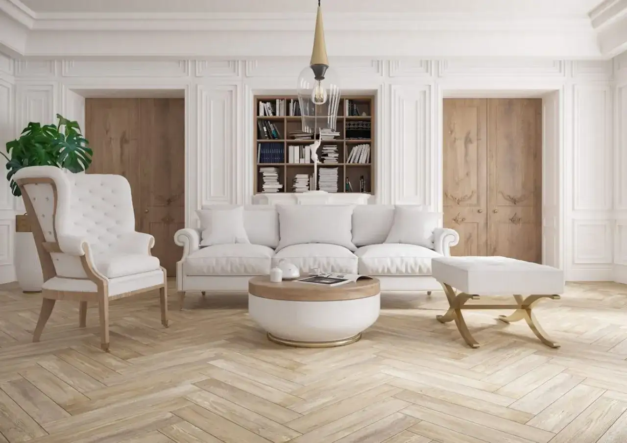 Elegancki salon z białymi meblami i sztukaterią na ścianach. W tle drewniane drzwi i regał z książkami.