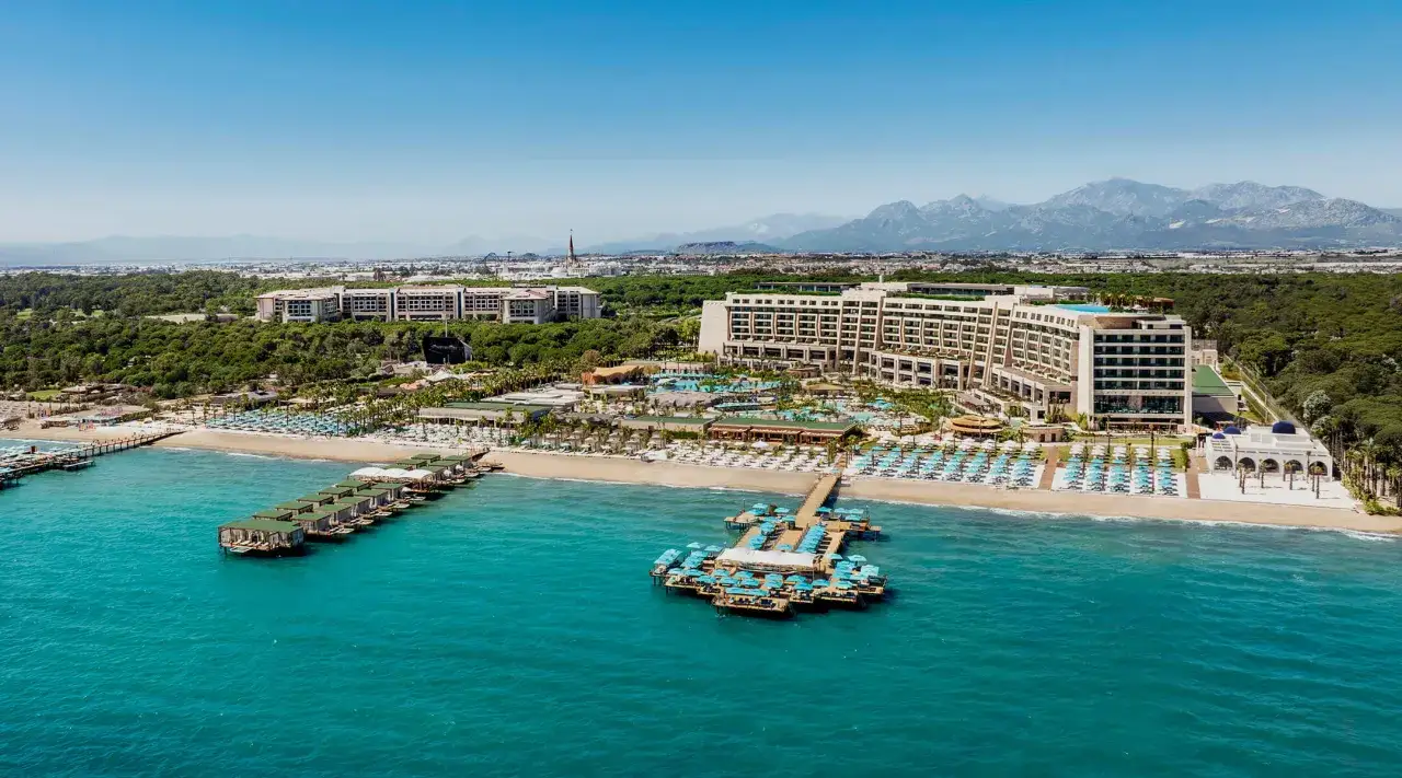 Luxuriöses Resort am Meer mit weitläufigen Pools, Strandliegen und Stegen. Das Regnum Carya bietet eine atemberaubende Aussicht auf das türkisfarbene Meer und die Berge.