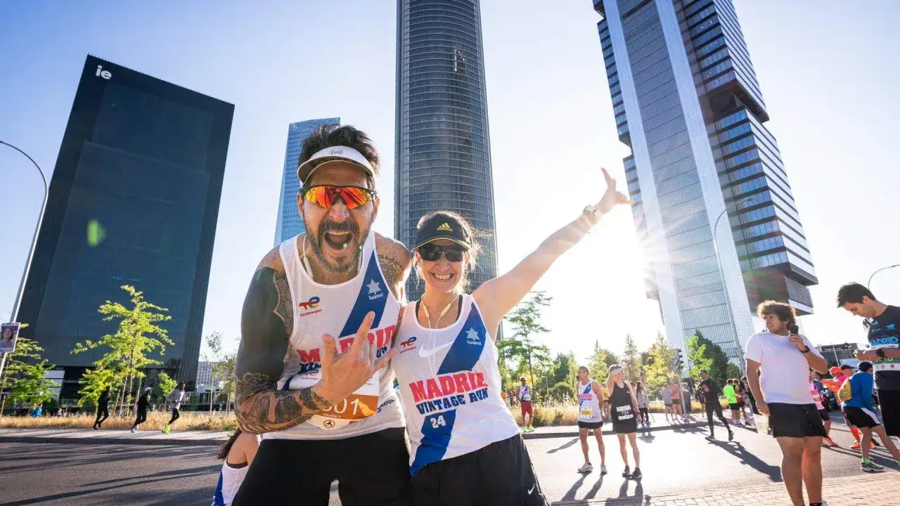 Pareja sonriente y animada en la Madrid Vintage Run, con rascacielos de fondo.