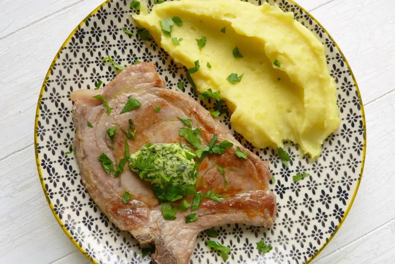 Perfekt gegartes Kalbskotelett sous vide mit Kr&auml;uterbutter und cremigem Kartoffelp&uuml;ree, garniert mit Petersilie.