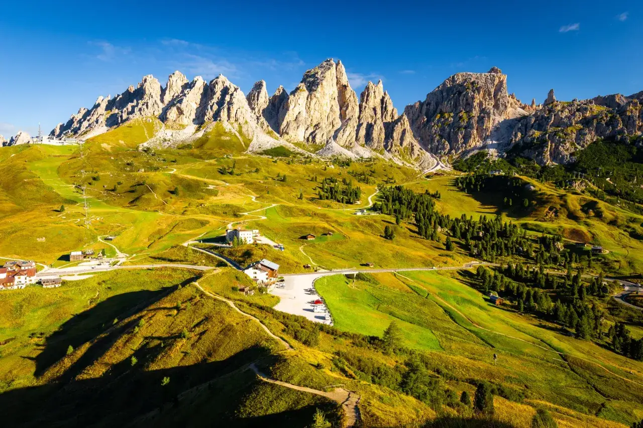 Paysage de montagne spectaculaire, avec des pics rocheux imposants et des pentes verdoyantes traversées par des sentiers. L'Alta Via 2 des Dolomites offre une vue imprenable.