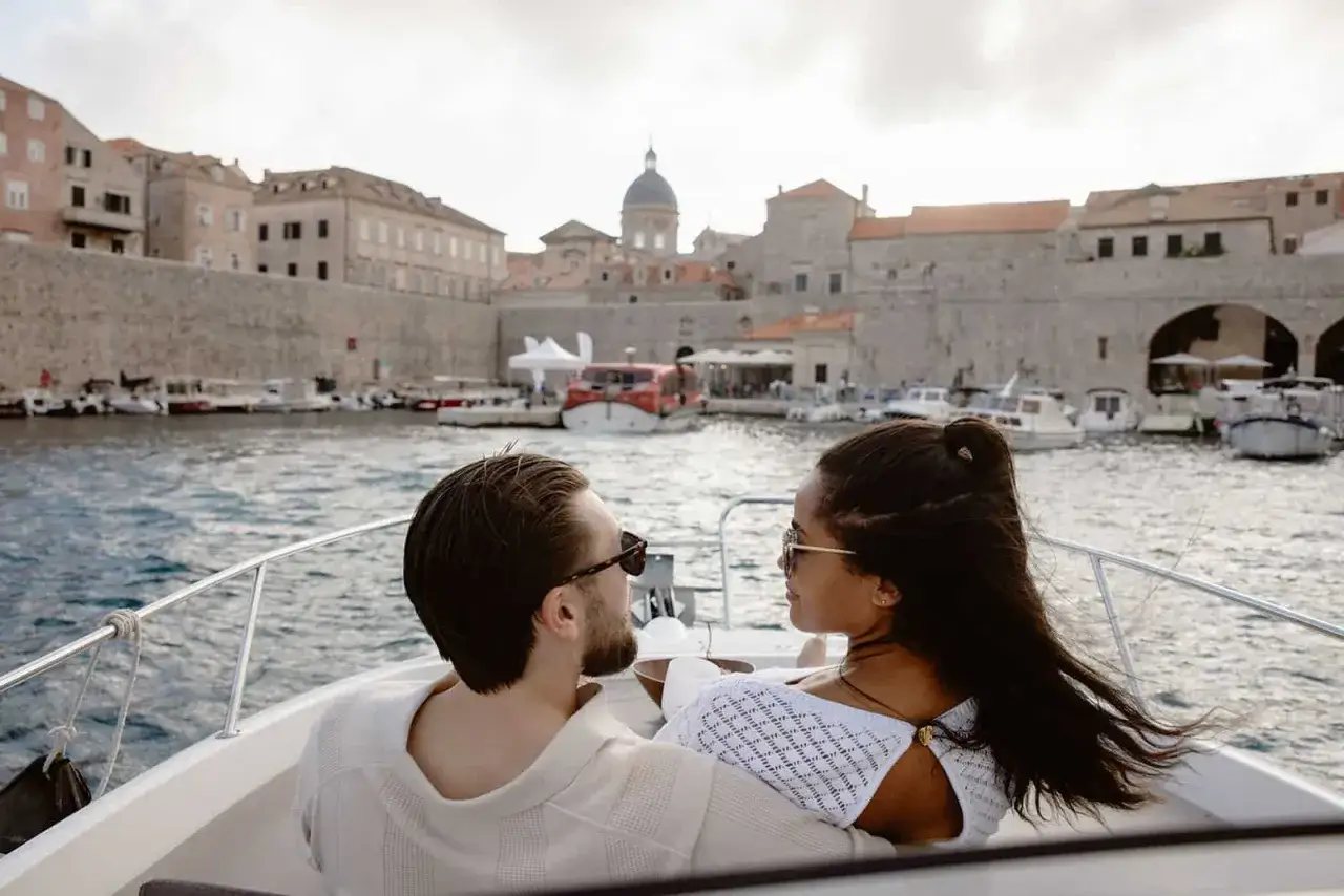 Par njuter av en båttur i Dubrovnik, Kroatien. Gamla stadens murar och hamnen syns i bakgrunden.