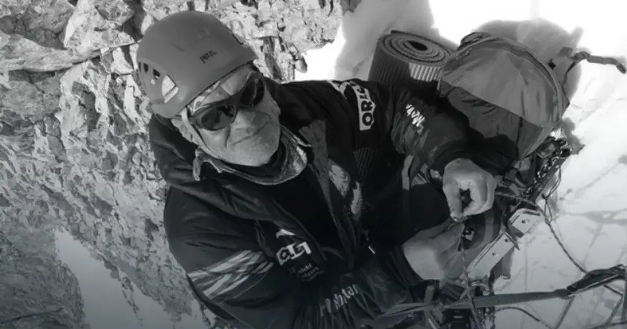 Alpinista w kasku i okularach przeciwsłonecznych, przygotowujący sprzęt. W tle skaliste zbocze, przypominające o tragedii na Broad Peak.