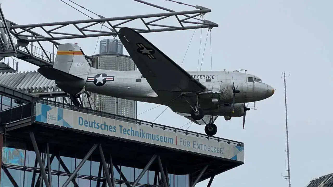 Samolot DC-3 wisi nad budynkiem z napisem