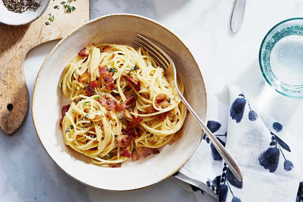 En skål med spaghetti carbonara, perfekt för att koka pasta. Krispigt bacon och örter toppar den krämiga pastan.