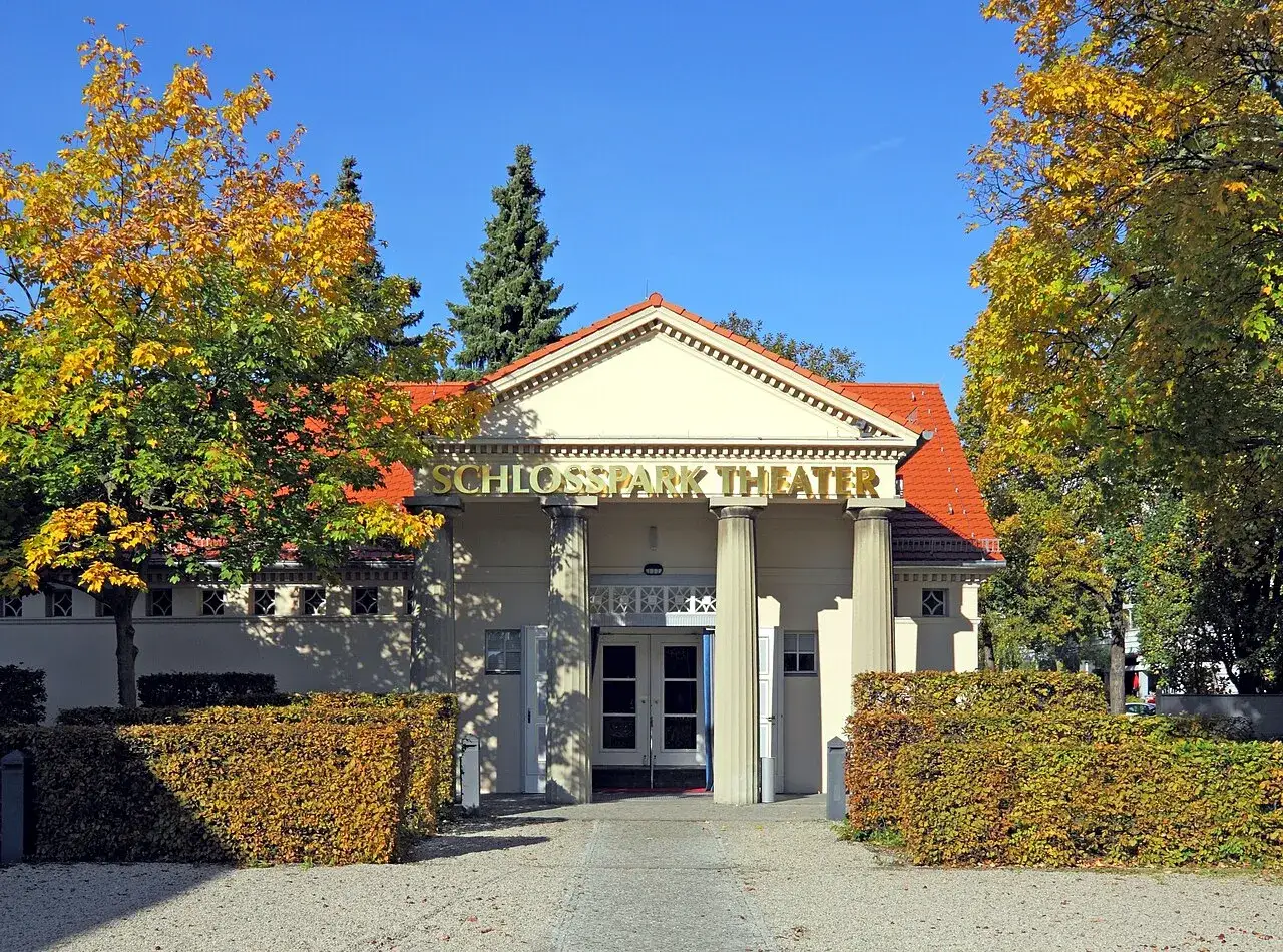 Das Schlosspark Theater im Herbstlicht, umgeben von B&auml;umen mit bunten Bl&auml;ttern.
