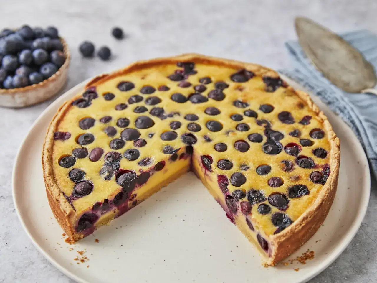 Ein köstlicher Heidelbeerkuchen mit Vanillepudding, belegt mit frischen Blaubeeren. Ein Stück fehlt bereits.