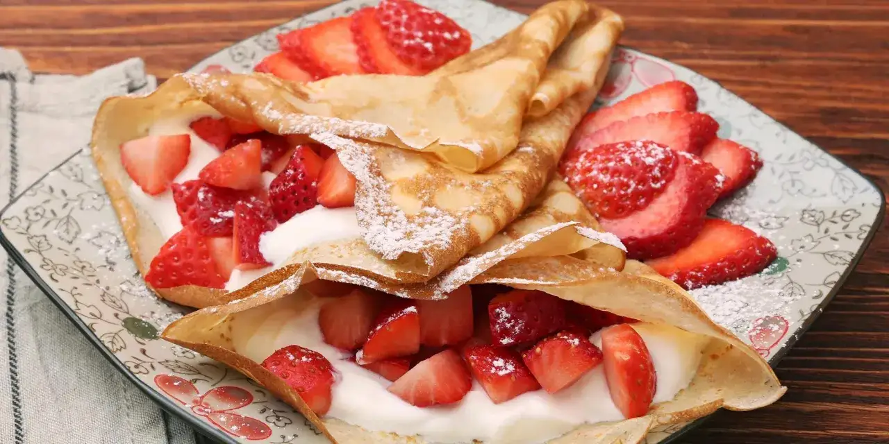 Zuckerfreie Crêpes gefüllt mit Sahne und frischen Erdbeeren, bestäubt mit Puderzucker. Ein Genuss für alle Sinne!