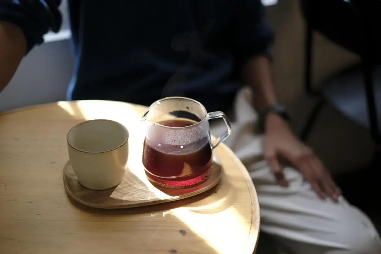 Un bicchiere di vetro con caff&egrave; speciali fumante e una tazzina vuota su un tavolino di legno.