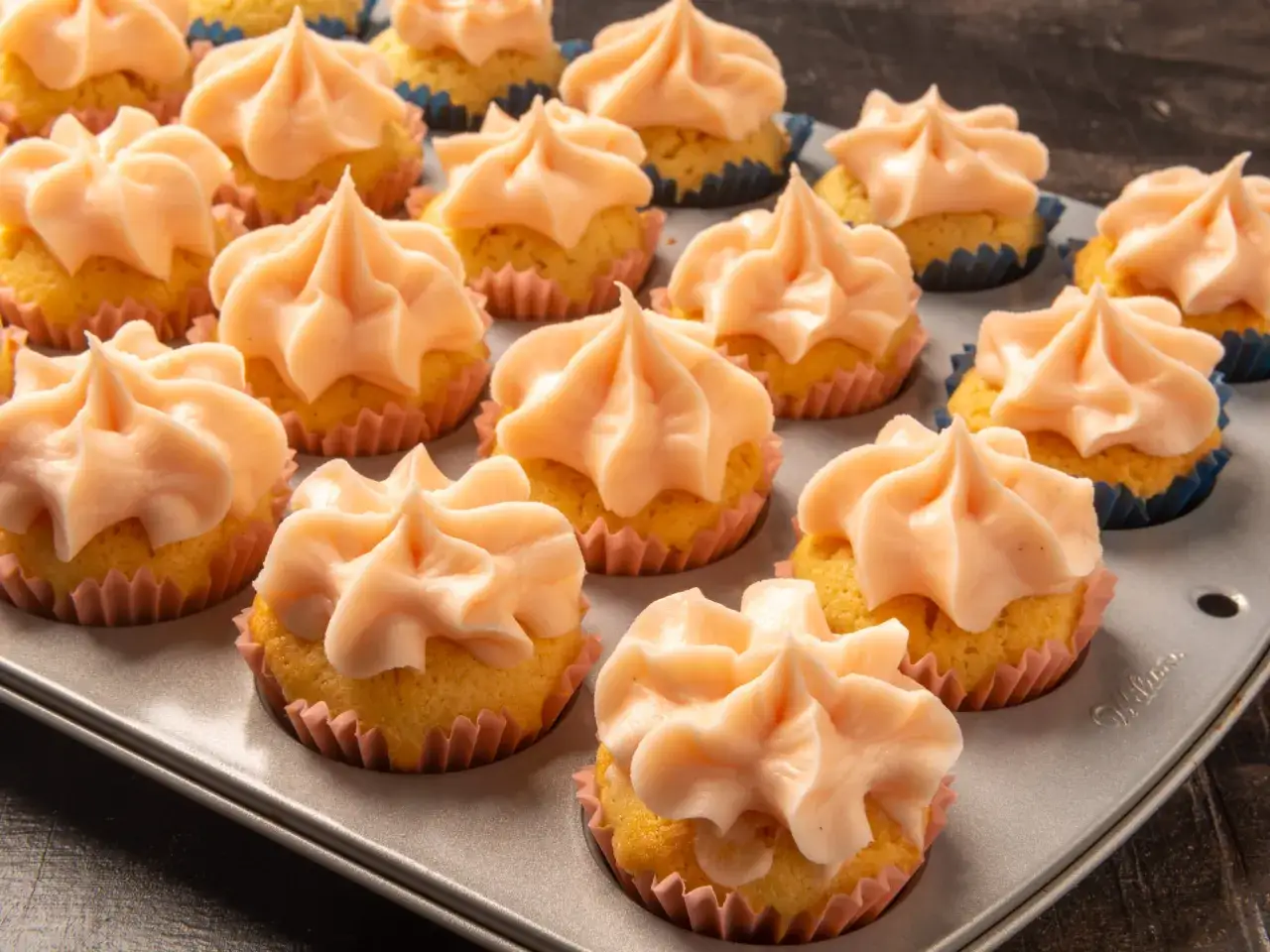Mini cupcakes med persikofärgad frosting i en muffinsplåt. Perfekt för ett enkelt mini cupcakes recept.