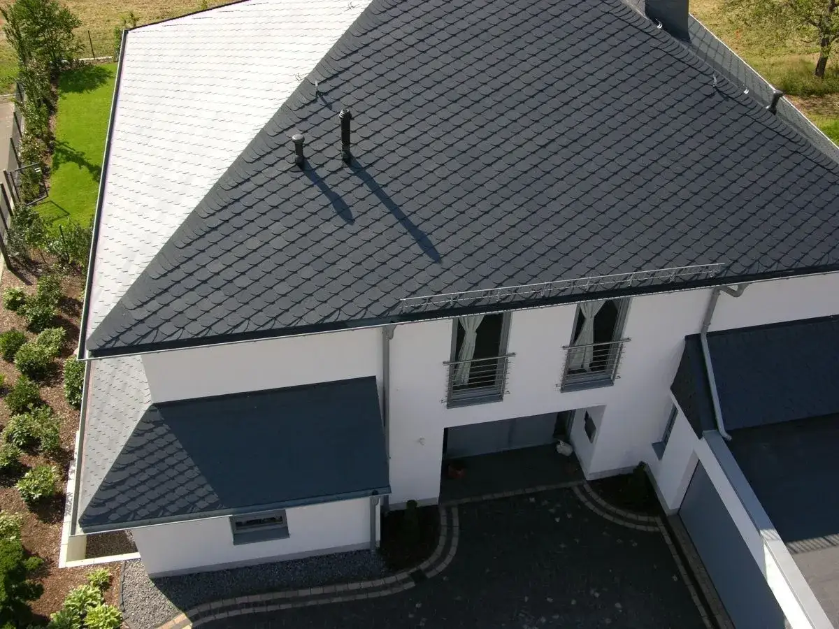 Dachansicht eines Hauses mit zwei verschiedenen Schieferdeckungen: ein Teil in dunklem Grau, der andere in hellem Grau. Verschiedene verlegemuster schiefer deckungsarten sind sichtbar.