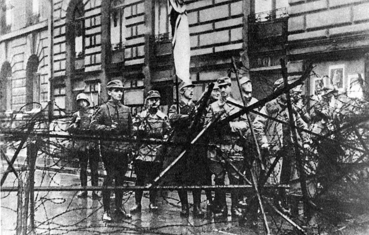 Soldaten sichern ein Gebäude mit Stacheldraht. Die Szene erinnert an den Putschversuch Hitlers.