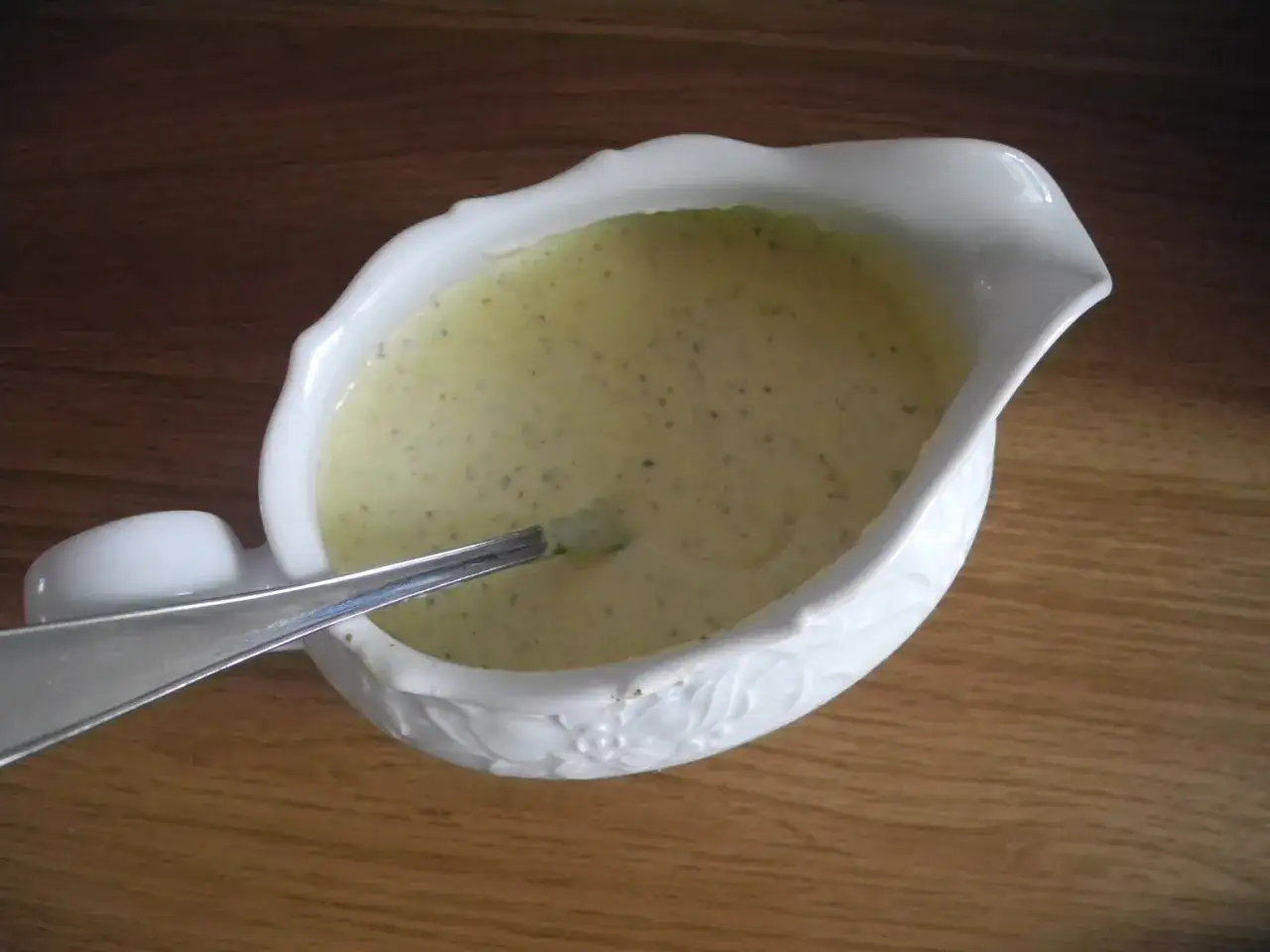 En vit såssnipa med en krämig, kall senapssås till korv. En sked ligger i såsen.