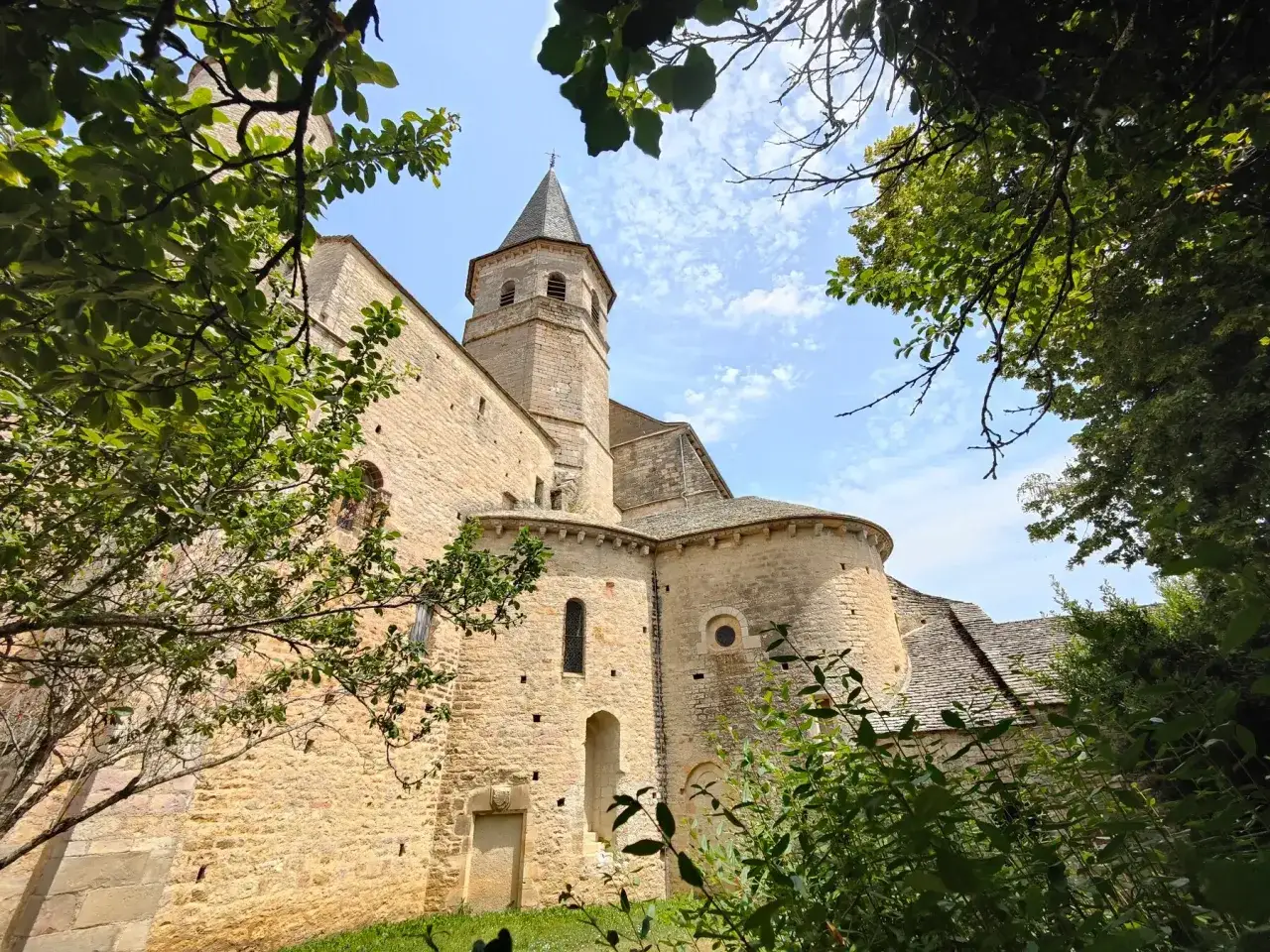 L'&eacute;glise romane de Villeneuve de Rouergue, baign&eacute;e de soleil, se dresse fi&egrave;rement sous un ciel bleu parsem&eacute; de nuages.