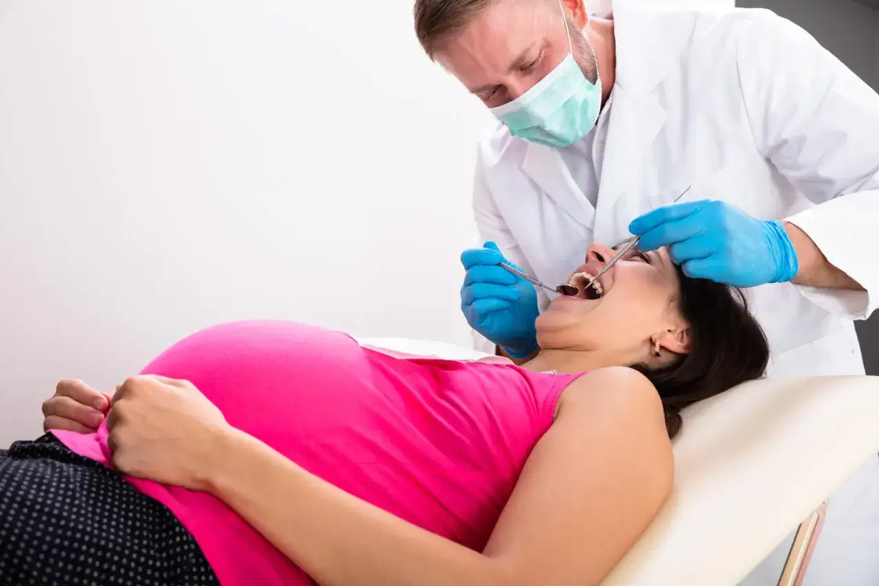 Dentysta bada zęby ciężarnej kobiety, która cierpi na ból zęba w ciąży.
