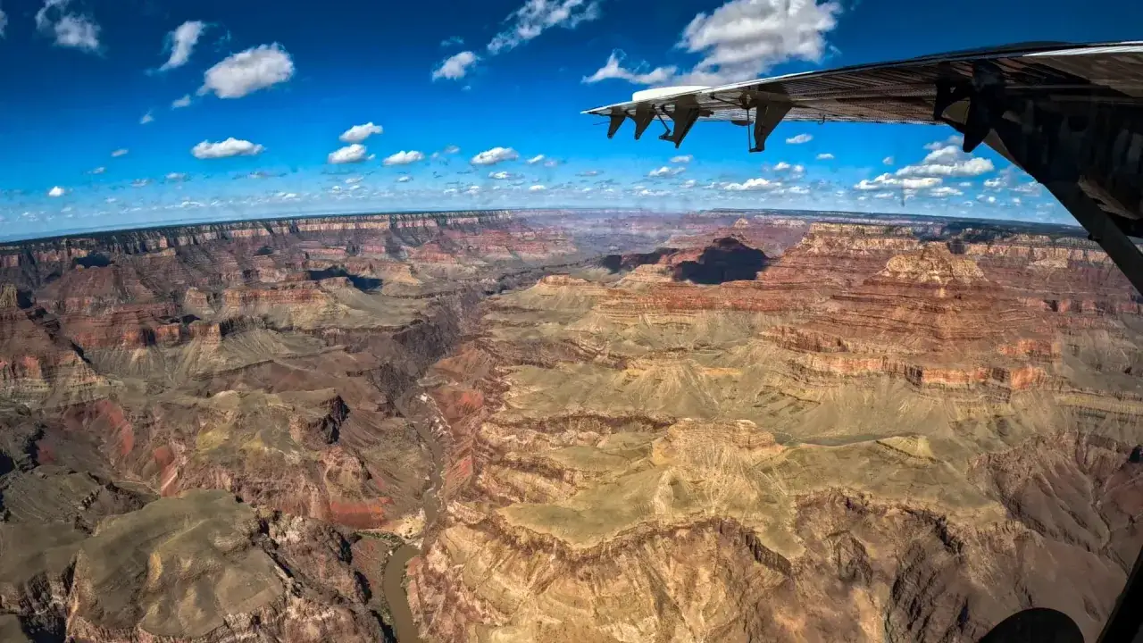 Niesamowity widok na **great canyon** z lotu ptaka. Skrzydło samolotu w kadrze, pod nim rozciąga się monumentalna, wielobarwna przepaść.