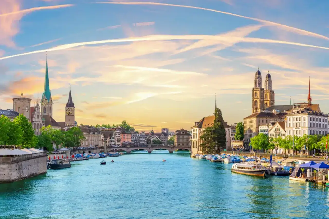 Zachód słońca nad Zurychem, z widokiem na rzekę Limmat, kościoły Grossmünster i Fraumünster. Idealne miejsce, by odkryć, zurych co warto zobaczyć.
