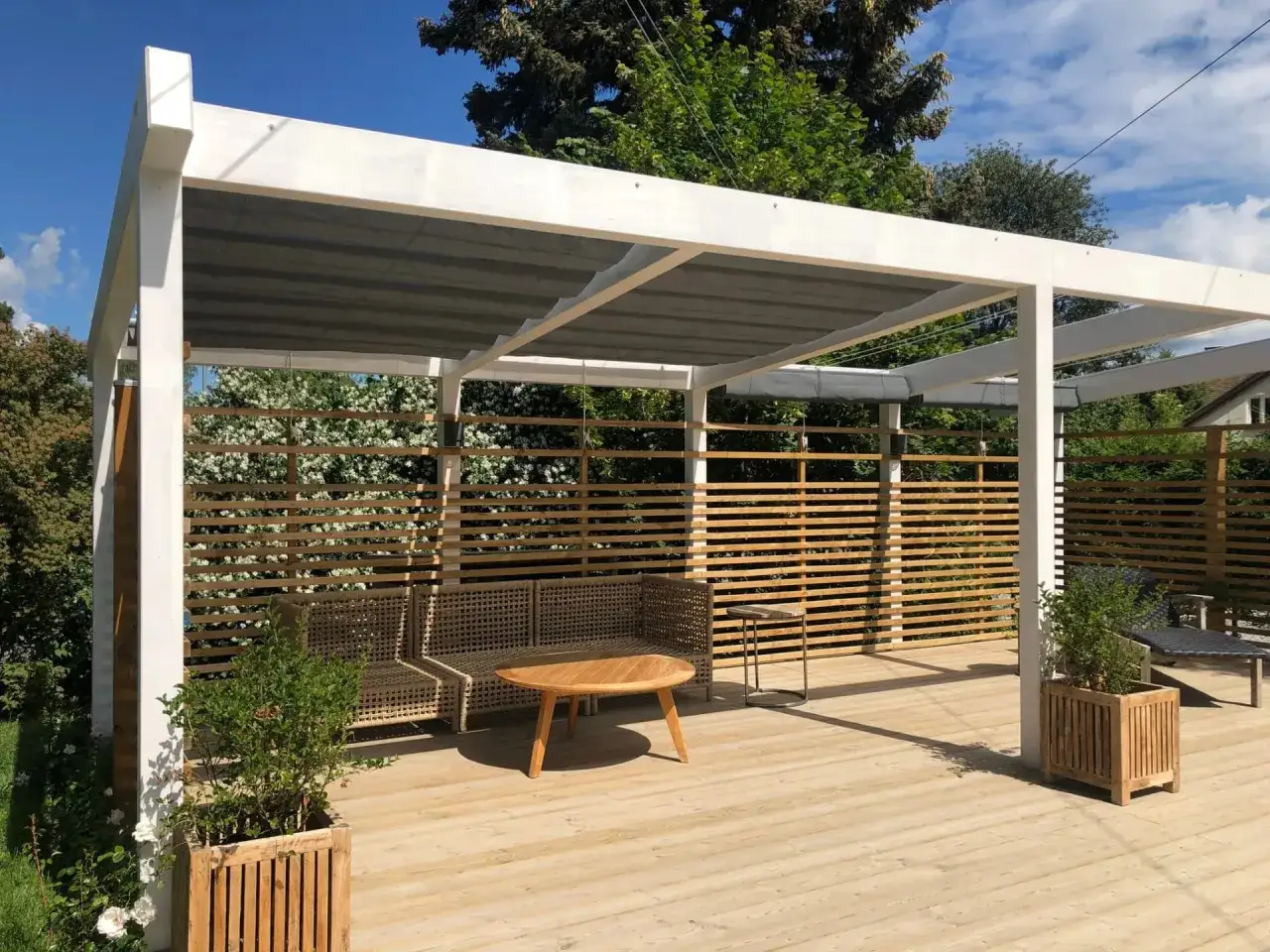 En mysig uteplats med pergola, soffgrupp och ett runt träbord. En fin **insektshotell placering** kan vara vid den träklädda väggen.