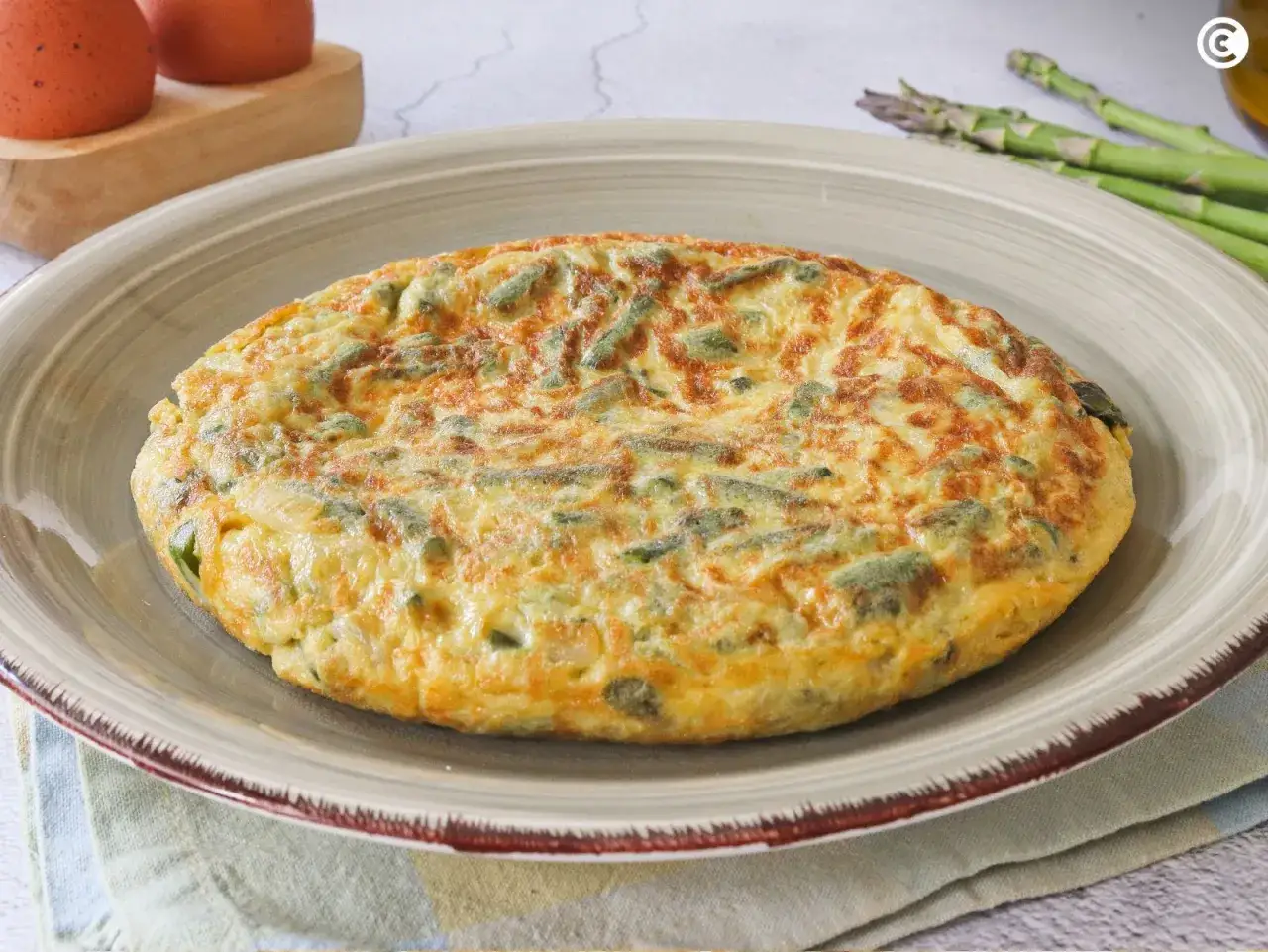 Tortilla de esparragos dorada y esponjosa, con trozos verdes de espárragos integrados en el huevo. Perfecta para un desayuno o cena ligera.