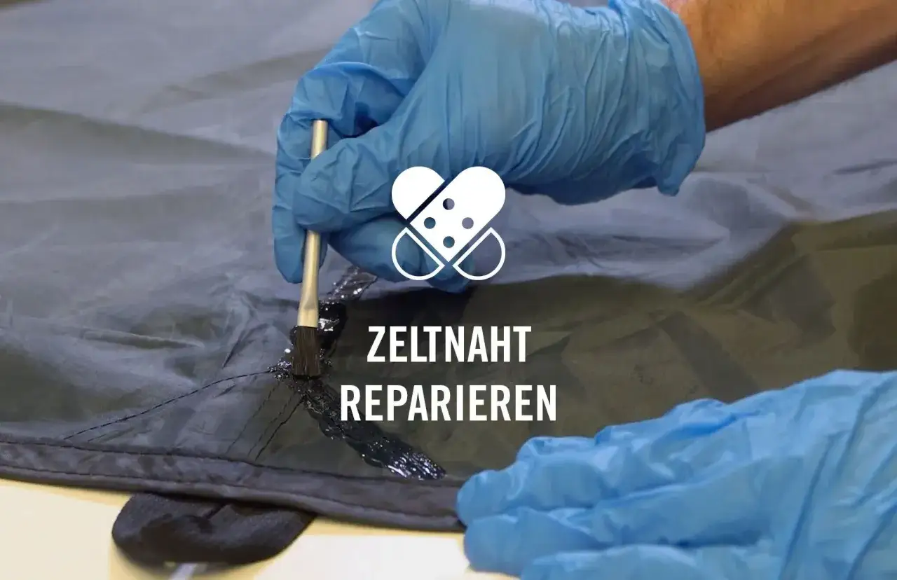 Mit blauen Handschuhen wird eine Naht am Zelt reparieren. Ein Pinsel tr&auml;gt schwarze Dichtungsmasse auf die Naht auf.