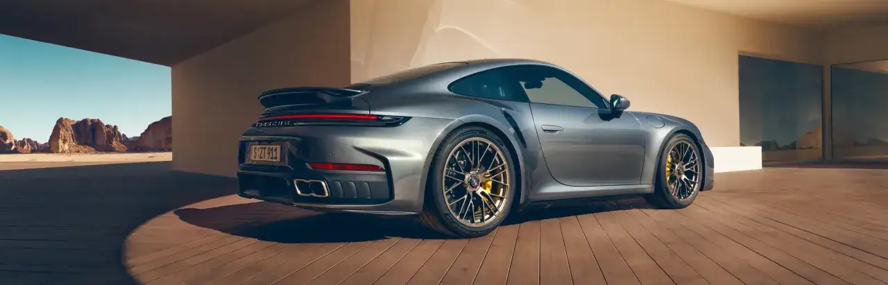 Szary Porsche 911 Turbo S z żółtymi zaciskami hamulcowymi stoi na drewnianym tarasie, z pustynnym krajobrazem w tle.