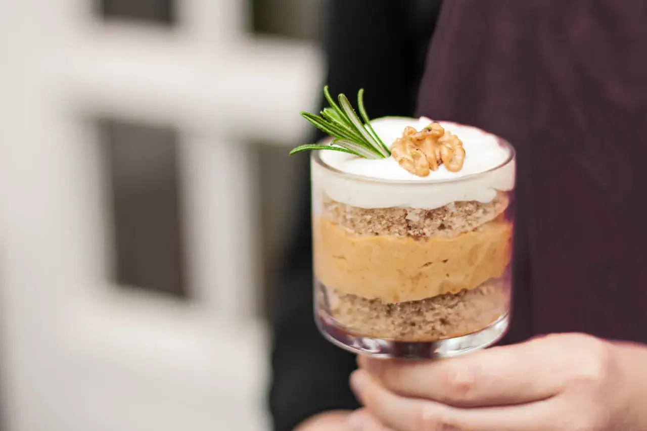 Ein Glas mit Schichten von Kuchen und cremiger Karamell-Mousse, garniert mit Rosmarin und einer Walnussh&auml;lfte.