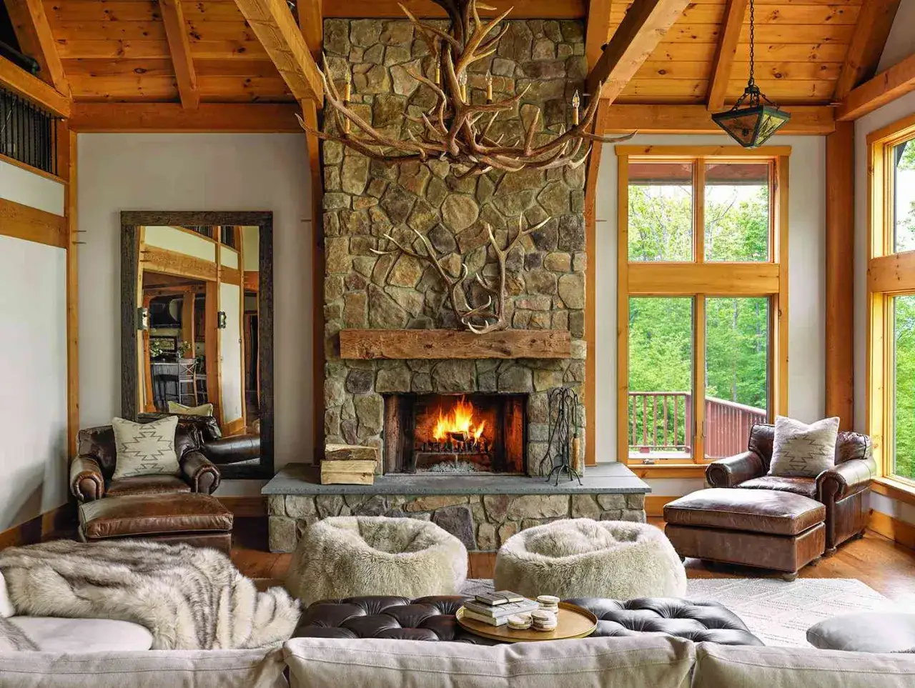 Cozy living room with a stone fireplace, antler chandelier, and leather furniture, embodying a warm rustic interior design.