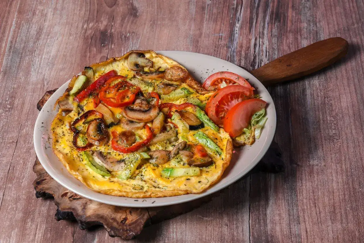 Pyszny omlet z pieczarkami, papryką i cukinią, udekorowany plasterkami pomidora. Idealny na śniadanie.